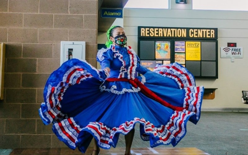 Luisa Valentin Pelagio inside in a hallway twirling her folklorico dance costume. Her folklorico dance costume is blue, red, and white.