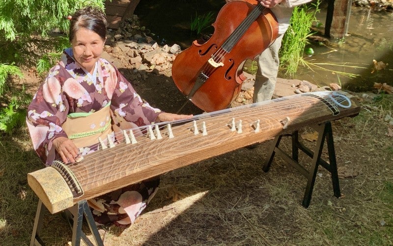 A woman, Masumi, sits with her koto. Beside her, a man stands with a cello