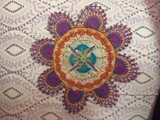 A woven rainbow colored flower pattern on white fabric. 