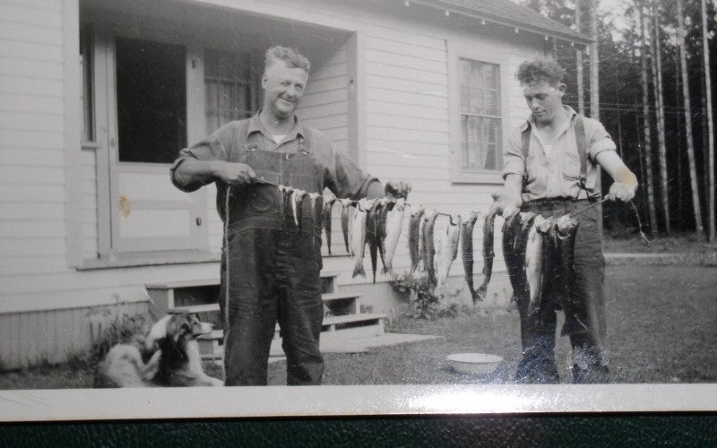 2 men holding up a line of fish that were recently caught
