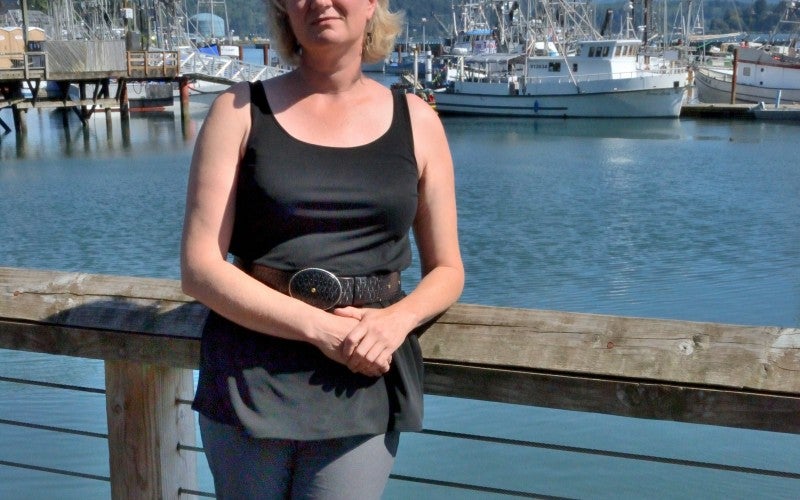 Laura Anderson standing on an ocean dock with some fishing boats behind her
