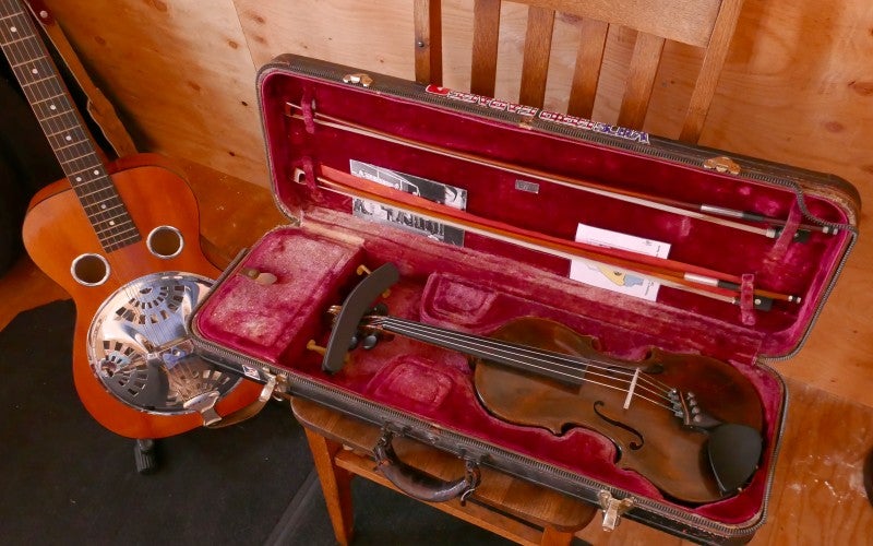 Photo of a violin in a case and a guitar on a floor stand