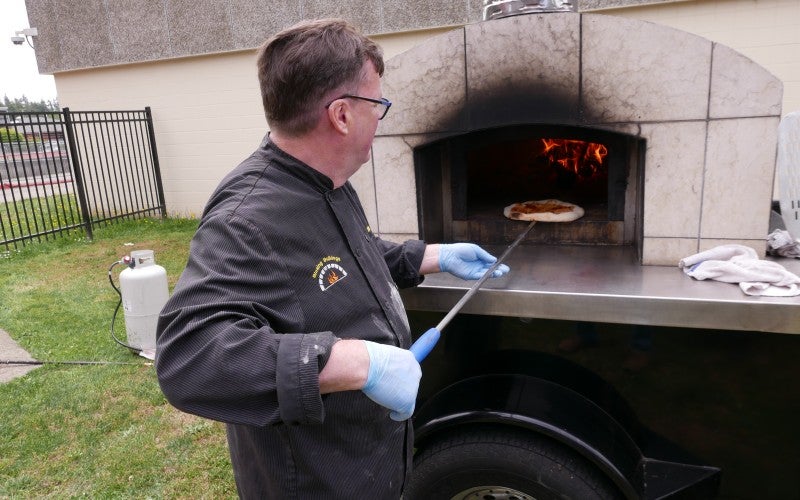 Frank Murphy placing a pizza in a woodfire oven outdoors