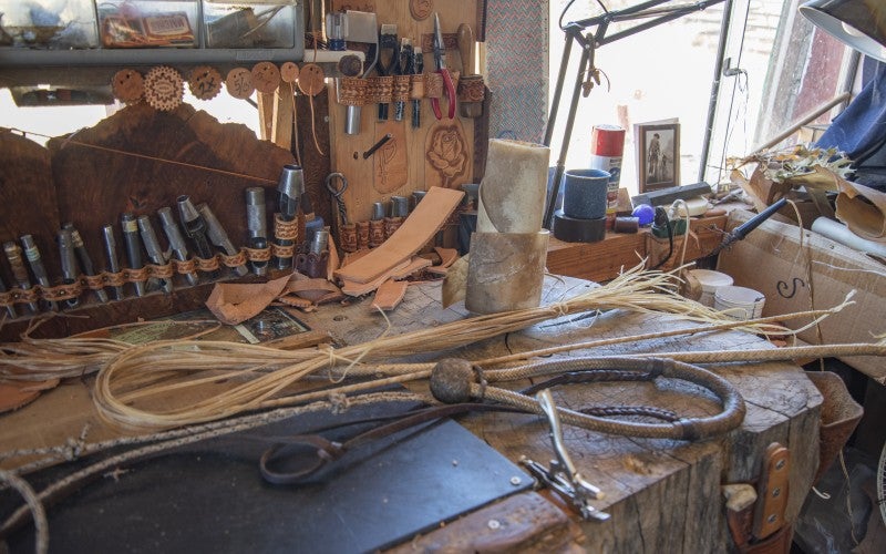Harris's work station. It is a wide table cut from a single slab of wood. Rawhide braiding tools are strewn over the surface in front of neatly organized metal carving tools.