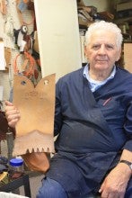 Mike Purves sits in a workshop holding a piece of boot leather and wears a navy blue shirt.