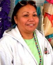 Sara Scott stands next to a white wire rack with crafted rawhide objects. She is wearing a lime shirt and a white hooded sweatshirt.