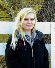 Callista Howell stands outside the Ft. Dalles Riders Club in front of a white fence. She wears a black sweatshirt over a light gray hooded sweatshirt.