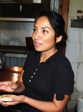 Maria Diaz stands in a kitchen and holds a small tortilla. She wears a black polo shirt.