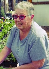 Linda Stephenson working with plants in her garden. She wears a gray t-shirt with white flowers on it.