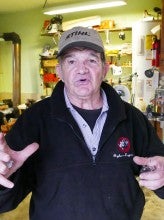 Luis Vidart expressively tells a story in front of several shelves full of tools. He wears a black jacket and gray baseball cap.