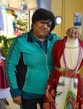 Lourdes Parra wears a blue jacket and stands next to a mannequin displaying a red and white traditional Mexican dress.