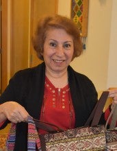 Maryam Monadi holds three woven handbags. She wears a red blouse and a black jacket .