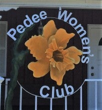 The Pedee Women's Club building. It is a red house with a white roof and white trim. The Club sign is rounded and has a daffodil on it.