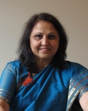 Nisha Joshi poses against a white wall, wearing a blue and gold sari.