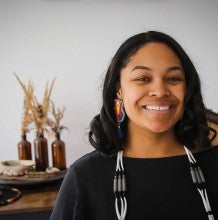 Eleeziaa, a woman with dark skin and dark shoulder length hair, smiles for a profile picture