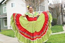 Luisa Valentin Pelagio wearing a folklorico dance cosutume that is red and yellow. She is standing outside.