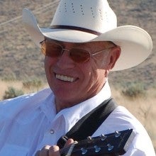 Lonnie in a white Cowboy hat playing his guitar. 