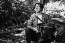 Brian O'hAirt sitting outside on a rock holding an accordion. The picture is in black and white.