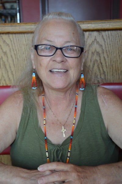 Margaret L. Johnson sits in a red booth. She wears a green tank top and a multicolored beaded necklace and earrings.