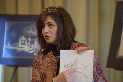 Marjan Anvari is speaking to an audience, holding a sample of work.