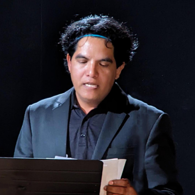 Juan Cervantes, a man in a blue suit, reads poetry with a black background