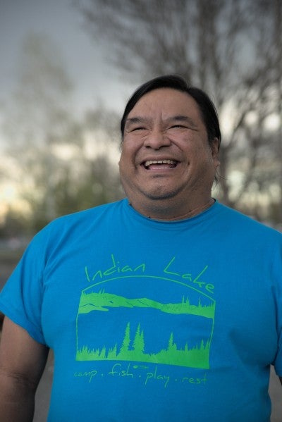 Michael Johnson standing outside with a tree in the background. He is wearing a blue shirt with green writing.