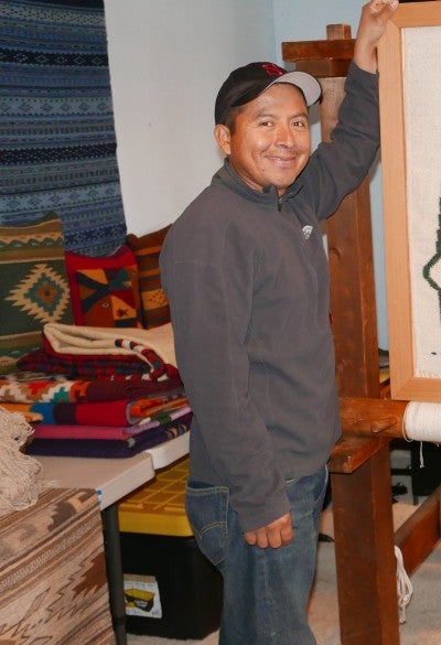 Francisco Baustista standing in his workshop wearing a baseball cap, jeans, and a grey jacket.