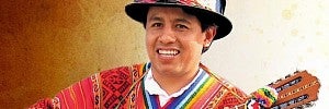 A guitar player with a friendly smile, wearing a festive hat and a traditional serape shawl.