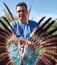 James Dionne stands outside and holds a brown feather creation and wears a blue shirt.