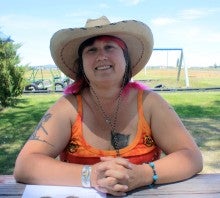 Becky Tocol sits outside at a wooden table in Christmas Valley, Oregon. She wears an orange tank top and a tan cowboy hat.
