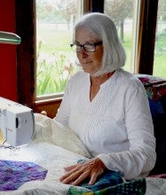 Colleen Blackwood sits at her sewing machine in Pendleton, Oregon and makes a colorful quilt. She wears a white long sleeved shirt.