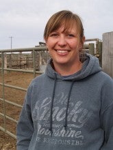 Jamie Wilson stands outside at her ranch in front of metal bars wearing a gray hoodie.
