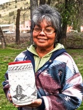 Bernyce Courtney stands outside and poses with a red, white, and black basket with frogs woven into it. She wears a red, blue, and white coat over a green sweater.