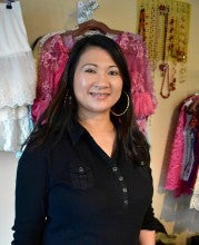 Portrait of Amara Sim in front of her Cambodian wedding clothing at Fina Salon in Beaverton, Oregon. She wears a black buttoned shirt.
