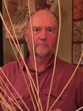 Andrew "Drew" Viles sits between strands of an unmade basket. He wears a red collared t-shirt.