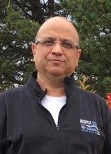 Ali Esteghlalian stands outside in front of trees. He wears a black jacket on top of a white shirt.