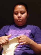 Grace Ann Kalama stretches a piece of fry bread dough. She wears a purple t-shirt.