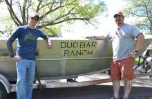 James Nash and Paul Pagano pose outdoors next to a boat named "Dugbar Ranch"