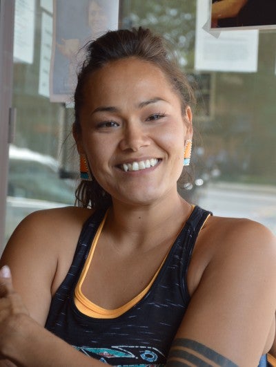 Portrait of Acosia Red Elk in Pendleton, Oregon. She wears a black tank top on top of an orange tank top.