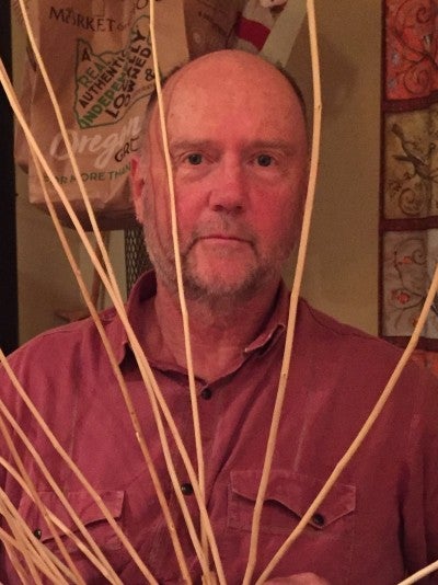 Andrew "Drew" Viles sits between strands of an unmade basket. He wears a red collared t-shirt.
