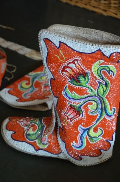 Leather beaded boots worn during jingle dancing. They have a floral design on a red and white background.
