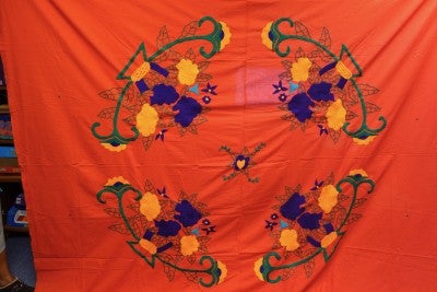 A bright orange sheet with blue, yellow, and green abstract flower embroidery.