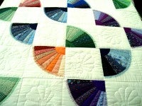 A colorful quilt with white squares and blue, green, and orange wedges.